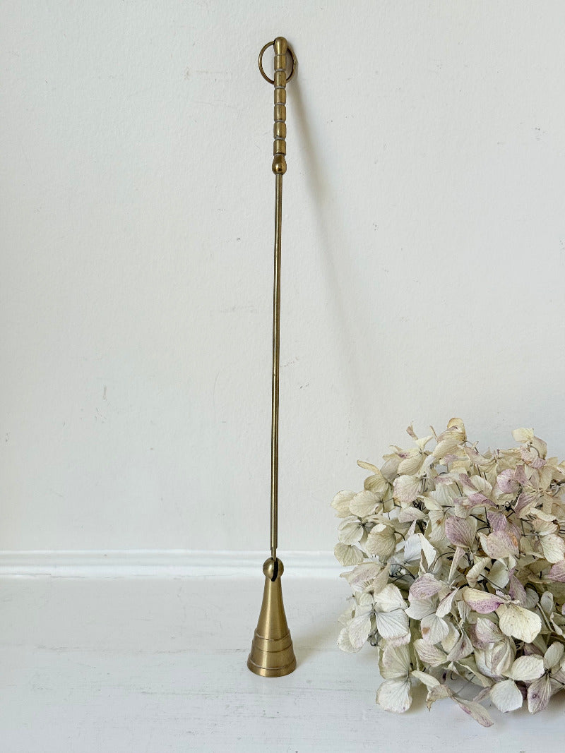 vintage brass candle snuffer with twisted handle and cone-shaped head photographed on white surface