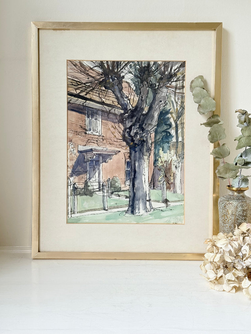 Framed vintage watercolour painting of a large tree and brick house, photographed on a white surface.