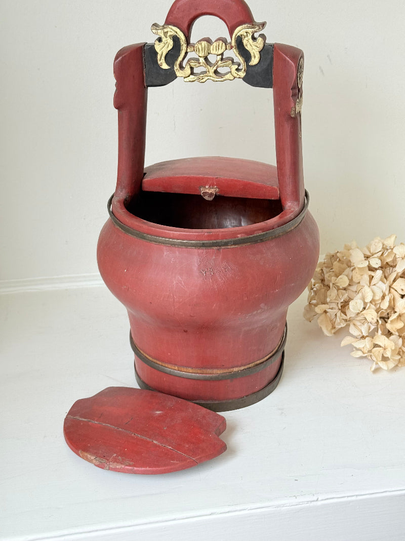 Vintage red painted wooden basket with upright handle and gold painted detail photographed on a white surface