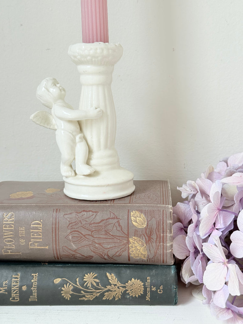 Vintage ceramic candlestick with angel figure and fluted column, cream glazed, styled with pink candle on white surface