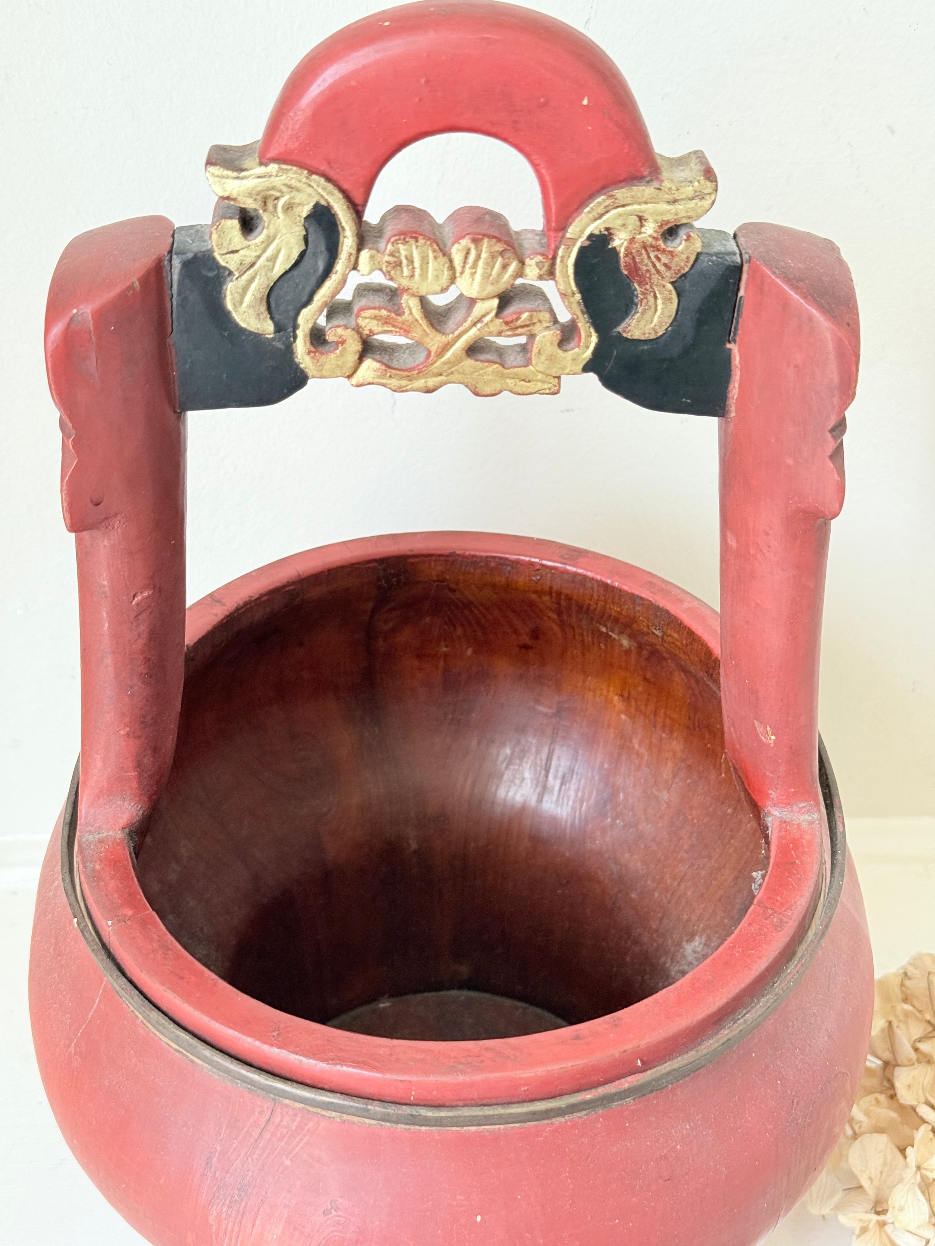 Vintage red painted wooden basket with upright handle and gold painted detail photographed on a white surface
