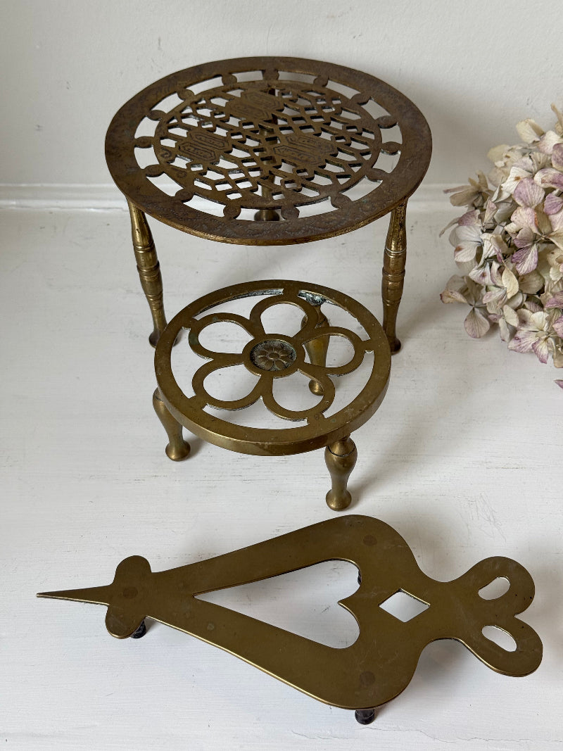 Vintage brass trivet trio with ornate cutwork designs and aged patina, photographed on a white surface