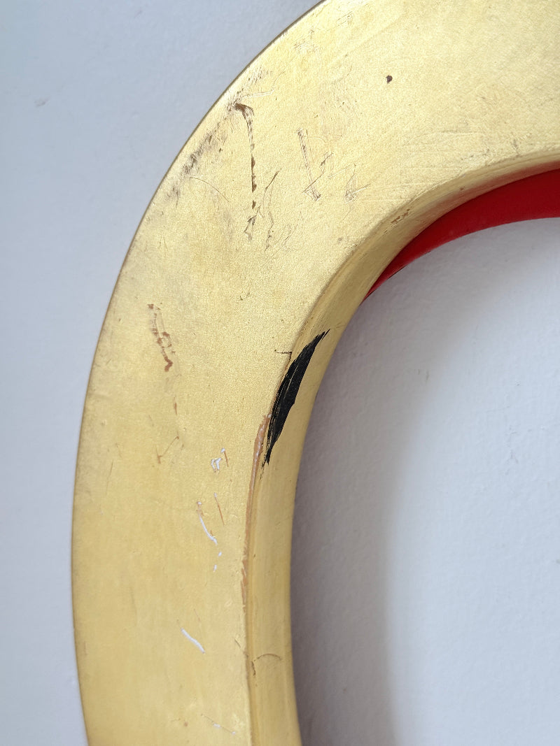 A close-up of a curved gold-colored frame or hoop with visible scratches and scuffs, showing a red interior lining against a light gray background.