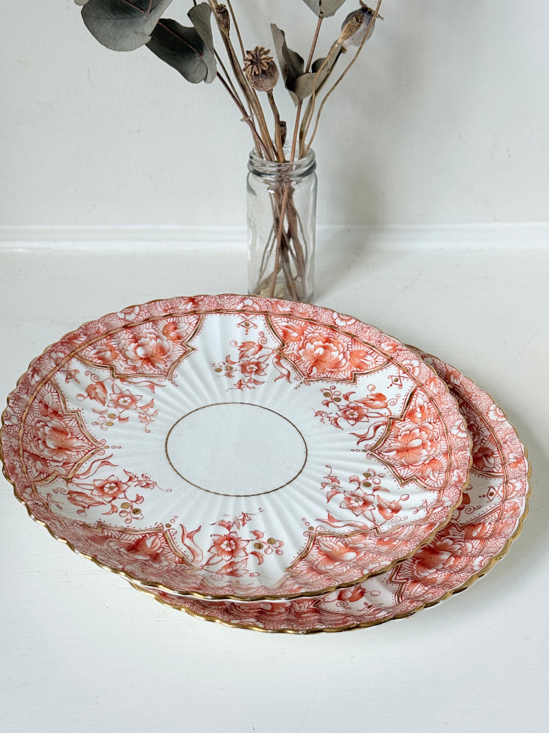 pair of vintage porcelain coral transfer plates with scalloped edges and gilt detail on white surface