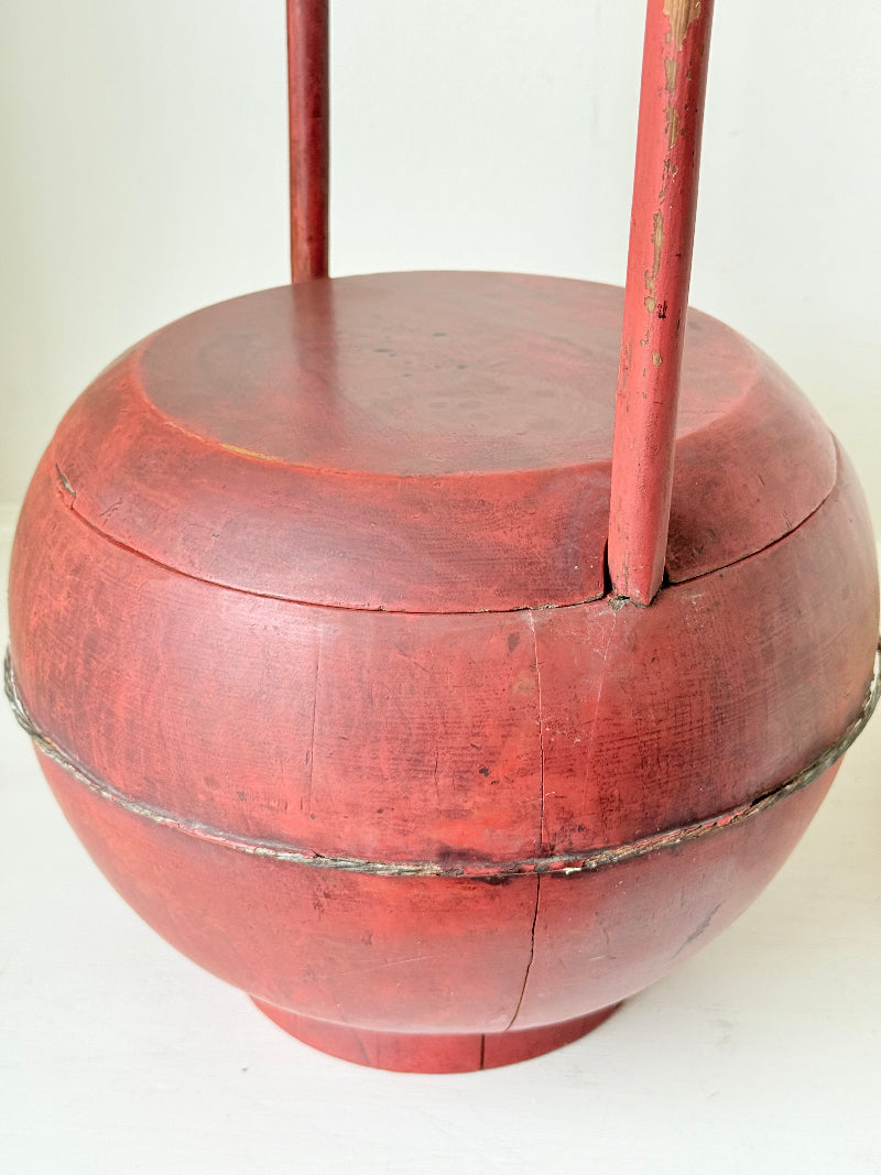 Vintage red painted wooden basket with tall curved handle and domed lid photographed on a white surface