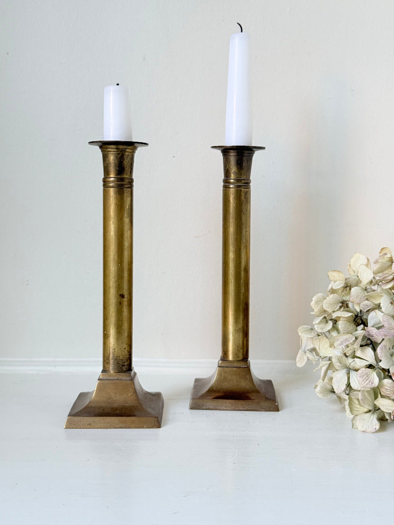 Pair of vintage brass candlesticks with square bases and white taper candles, styled on a white surface beside dried hydrangeas.