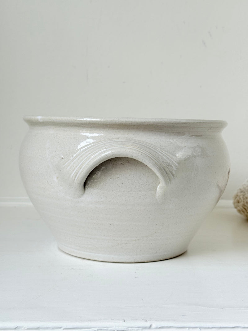 Large studio pottery bowl with hand-painted grape motif and side handles, photographed on a white surface