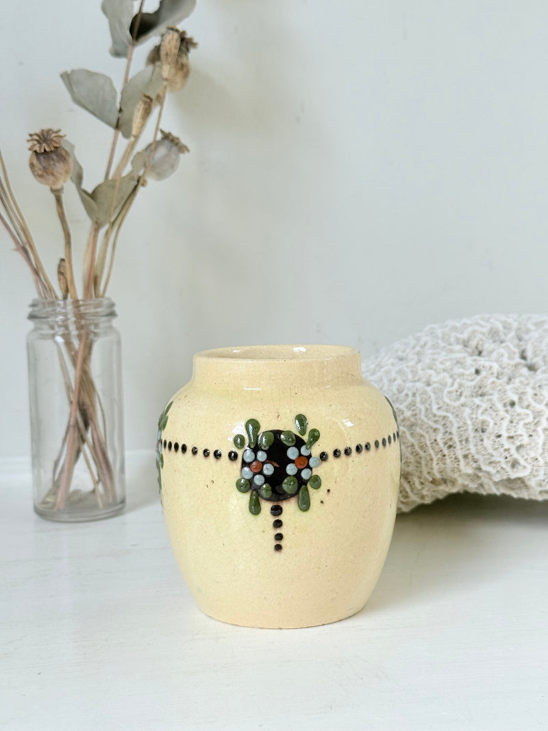 Cream studio pottery decorative pot with raised green floral motif, photographed on a white surface