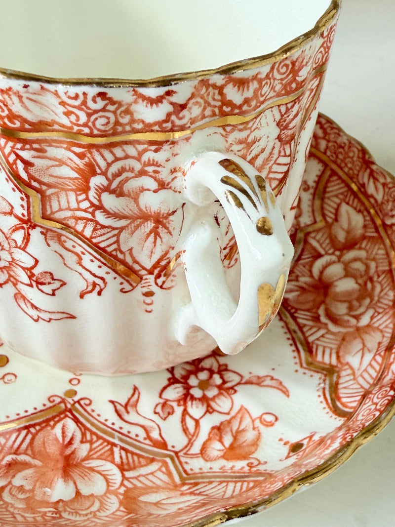 Vintage coral transferware coffee cans and saucers with scalloped edges and gold accents, set of ten, styled on a white surface.