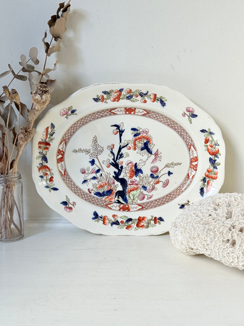 Vintage oval serving platter with chinoiserie style blue and red pattern photographed on a white surface