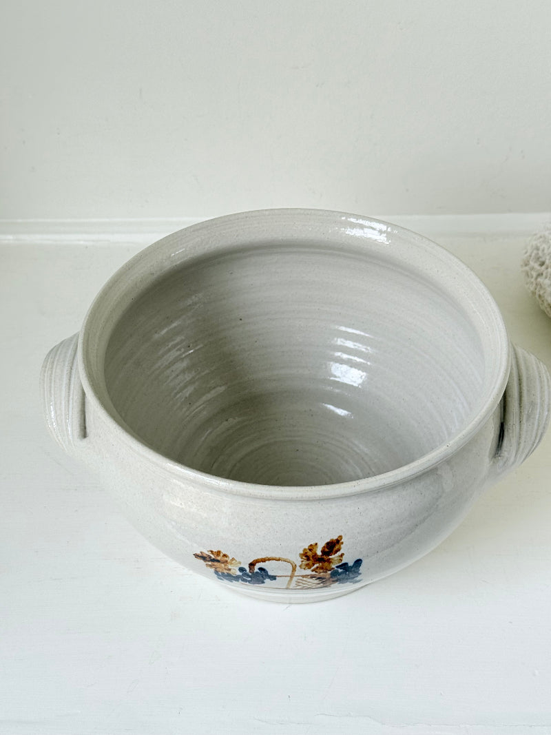 Large studio pottery bowl with hand-painted grape motif and side handles, photographed on a white surface