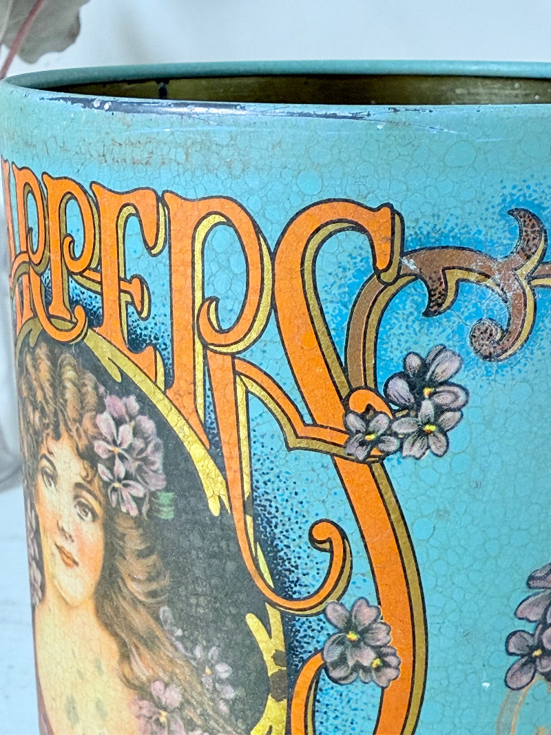 Vintage turquoise and gold metal sweet tin with Art Nouveau woman portrait photographed on a white surface.