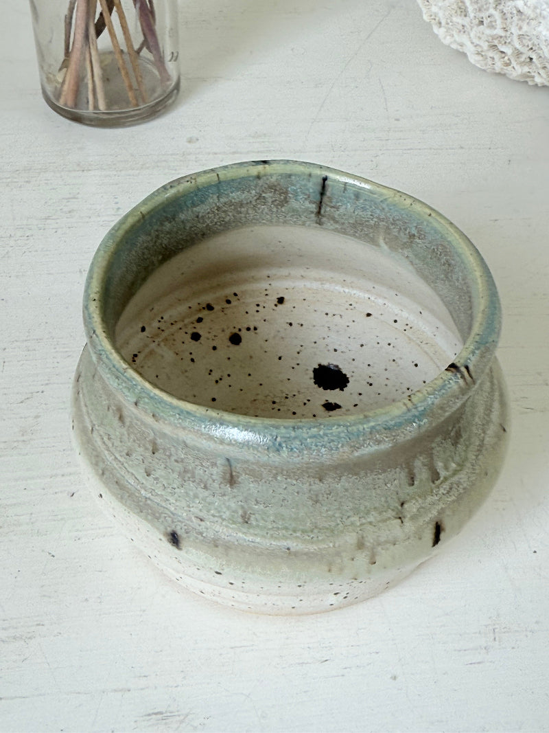 Studio pottery olive pot with soft green and cream glaze, photographed on a white surface