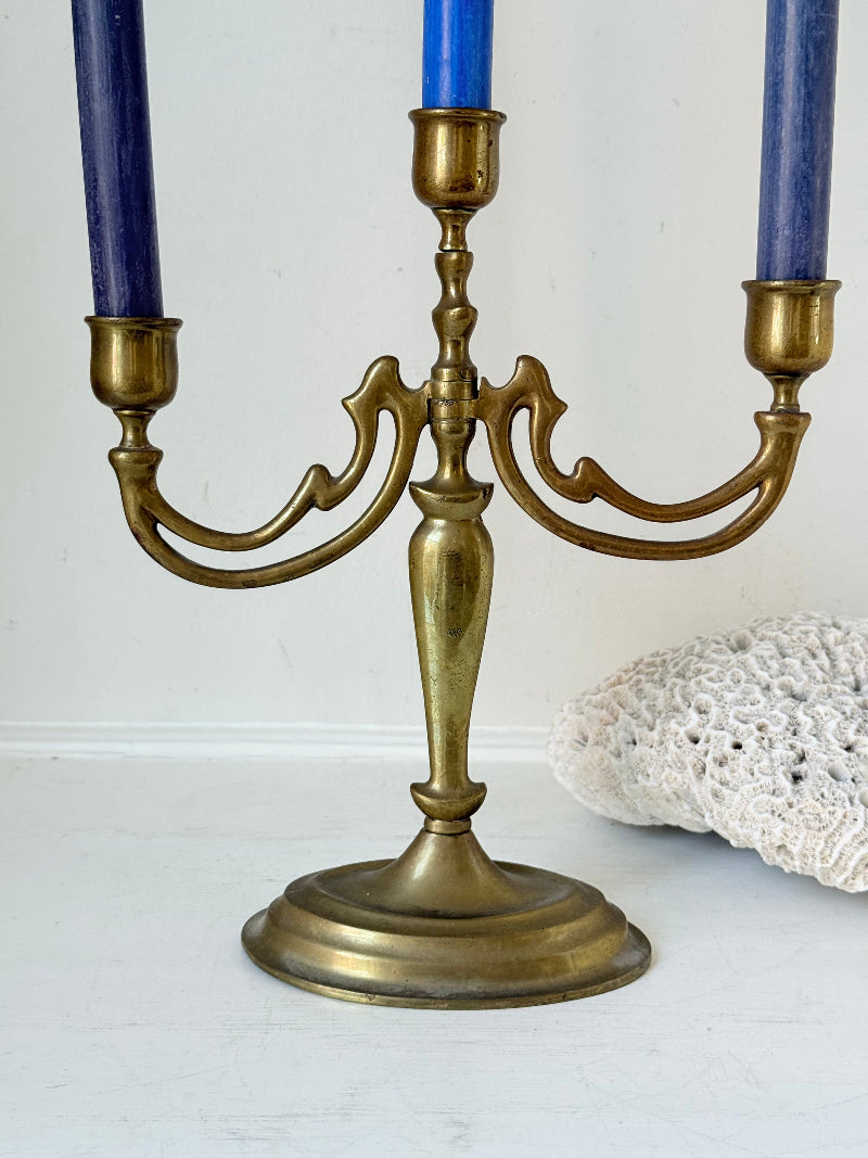 Vintage brass three-arm candelabra with curved arms and soft patina, photographed on a white surface