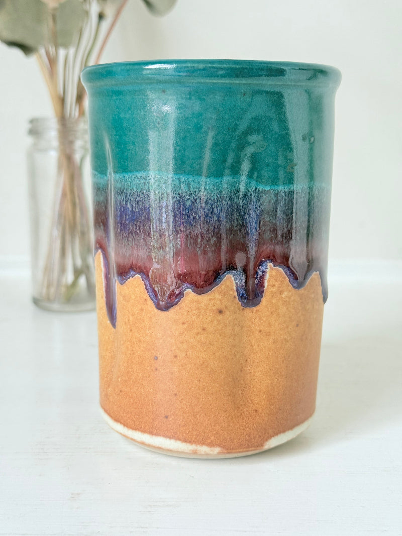 Studio pottery pen pot with teal and plum drip glaze, photographed on a white surface