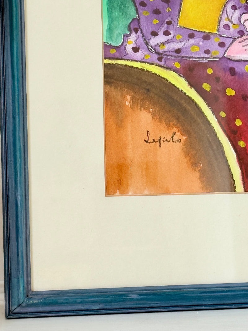 Original watercolour portrait of Pamela in blue frame, vibrant interior scene, photographed on white surface