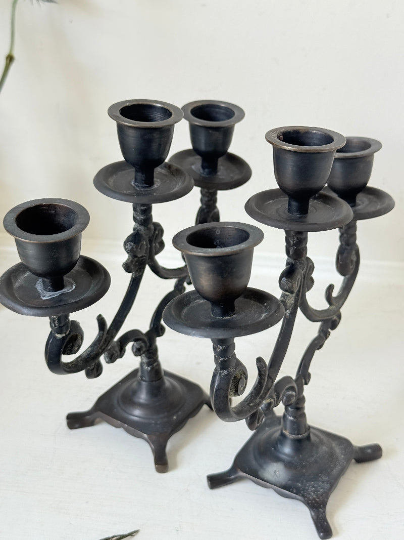 Pair of vintage brass three arm candelabra with scrolling arms and aged patina, photographed on a white surface