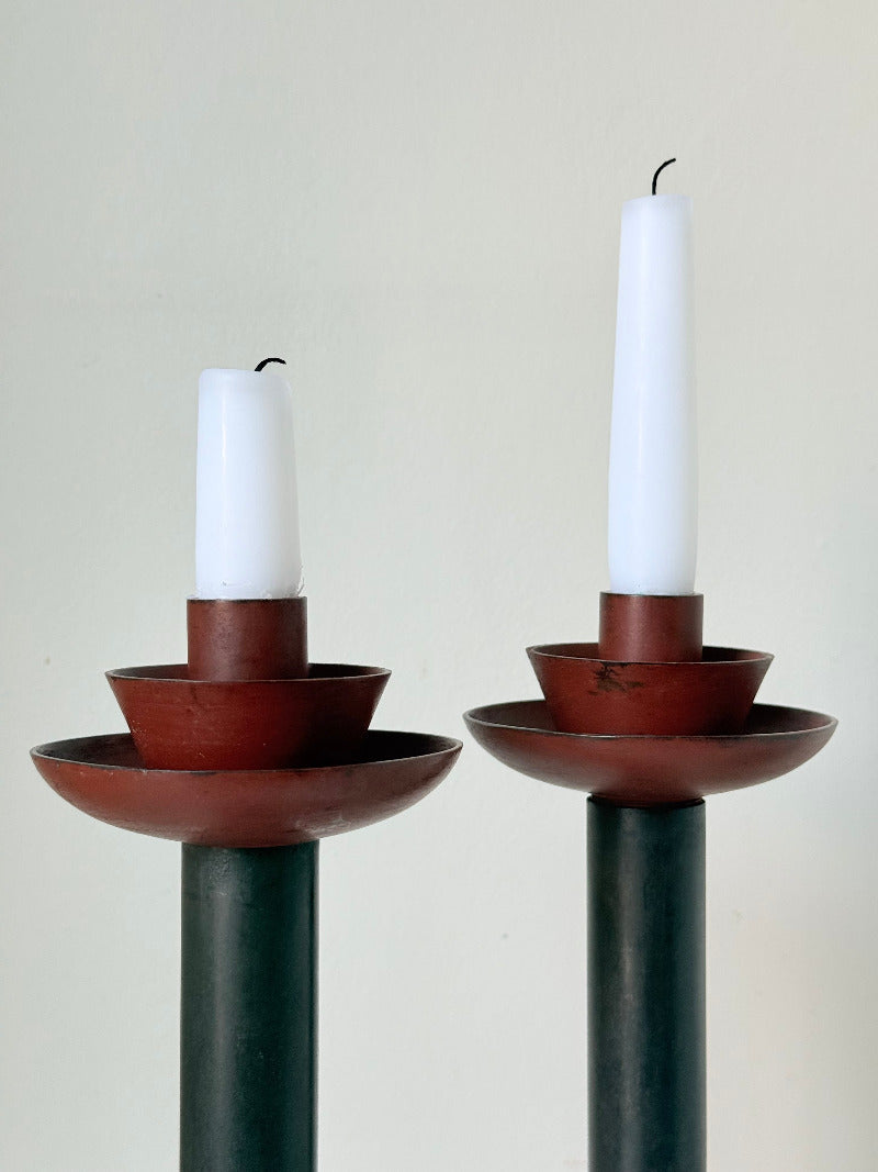 Pair of tall vintage metal candlesticks in black and burgundy, styled with white taper candles on a white surface.