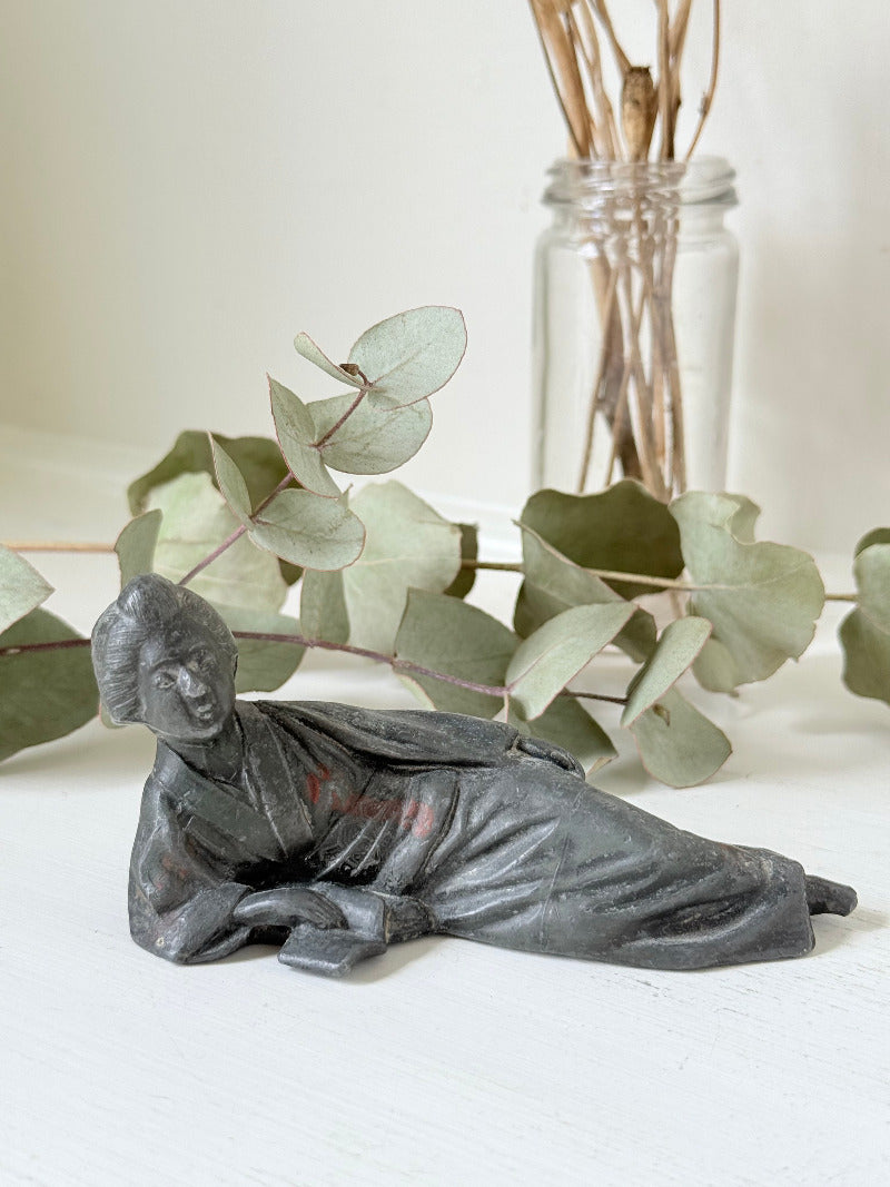 antique japanese bronze reclining lady with impressed marks to base photographed on white surface with foliage background