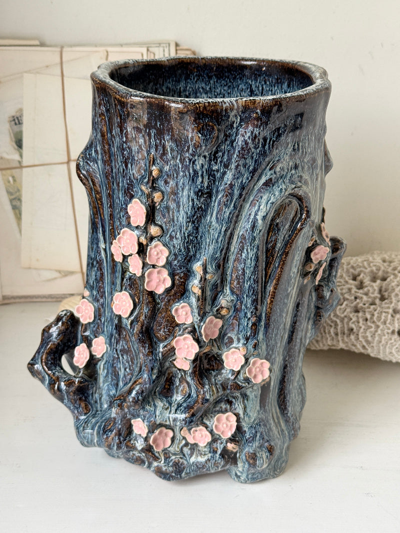 Large ceramic tree trunk vase with applied pink cherry blossom detail, textured bark form and dark drip glaze