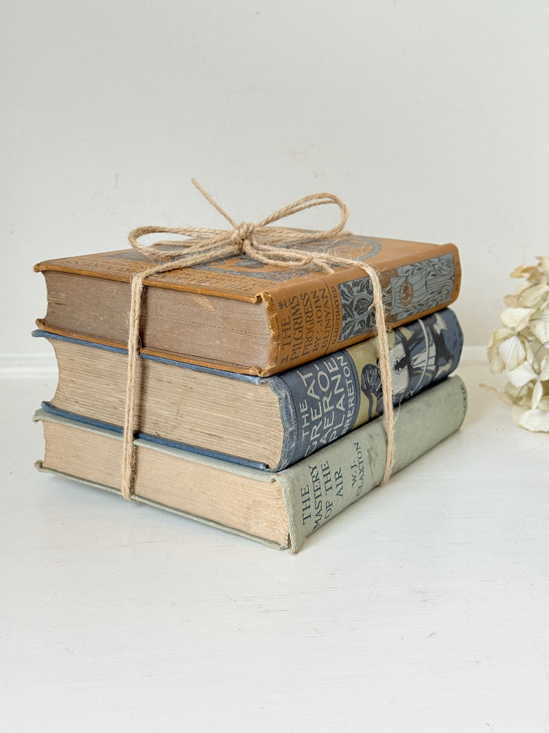 Vintage decorative book bundle in blue, grey, and ochre tied with twine, photographed on a white surface