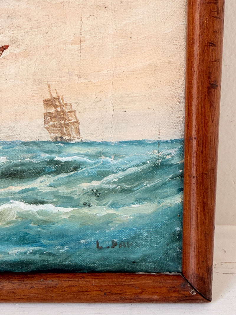 Close-up of a framed painting showing a seascape with blue-green ocean waves and a sailing ship under a pale sky, bordered by a warm brown wooden frame.