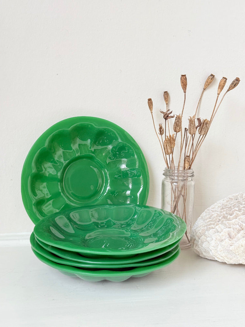 set of five vintage green pressed glass plates with decorative pattern, photographed on a white surface with dried flowers