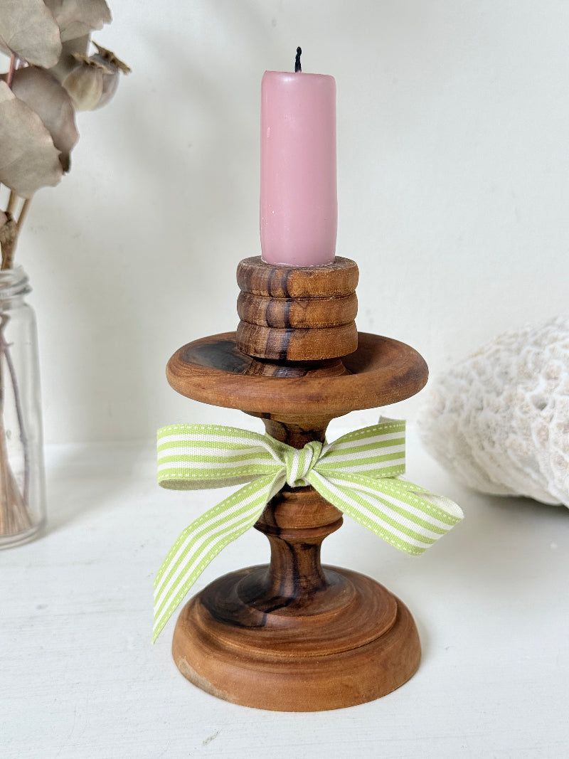 Vintage olivewood candlestick photographed on a white surface, turned wooden stem with warm grain and wide base holding a pink taper candle