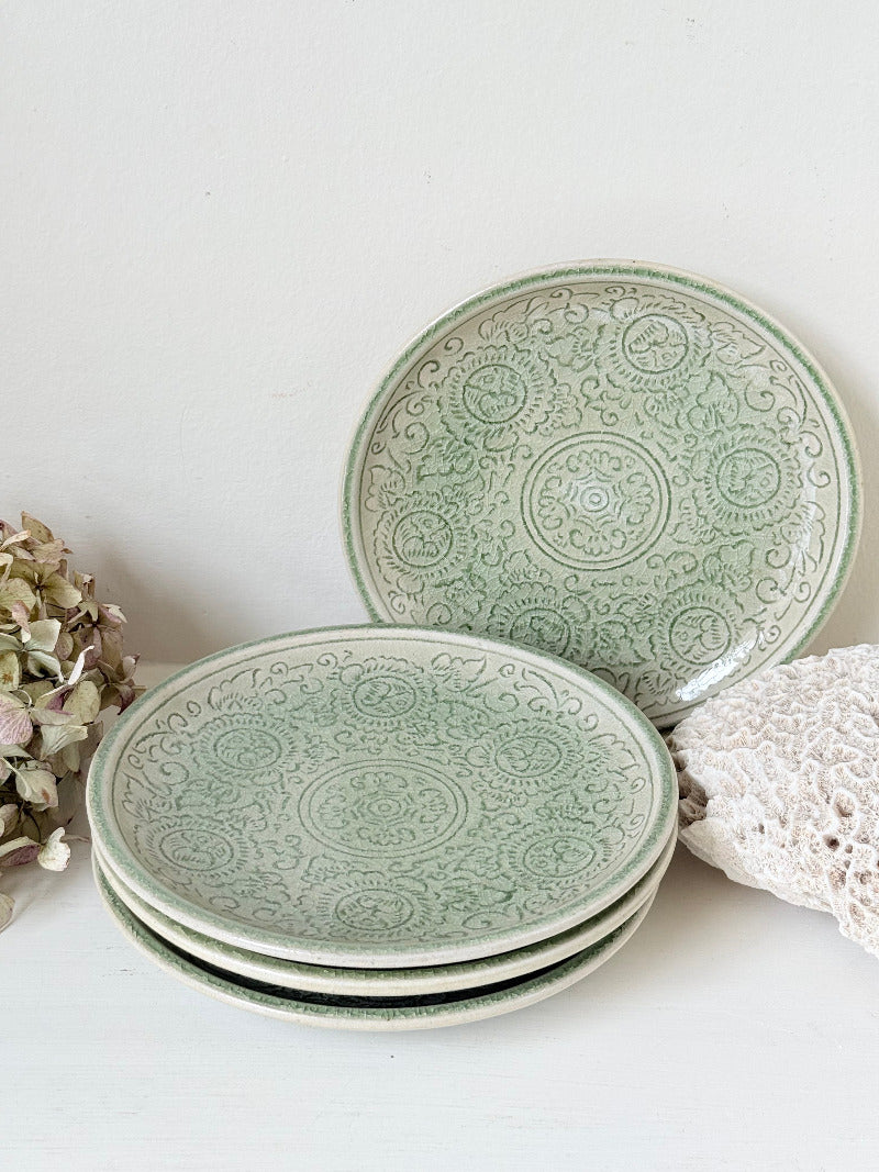 Set of four Thai stoneware plates with soft green celadon glaze on white surface