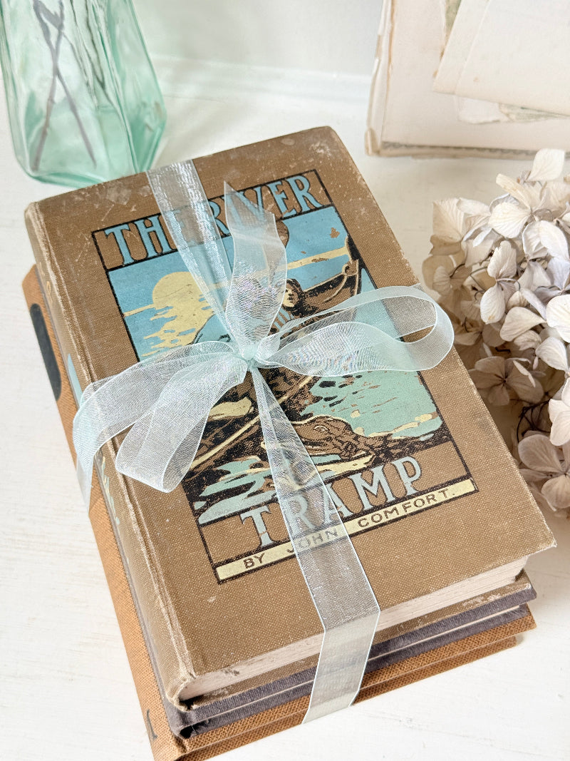 Bundle of vintage hardback books in brown, tan and navy tied with a pale blue satin ribbon for shelf and table styling