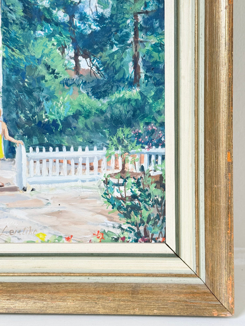 Oil on board painting of a girl in a yellow dress outside a cottage with picket fence, framed, photographed on a white surface
