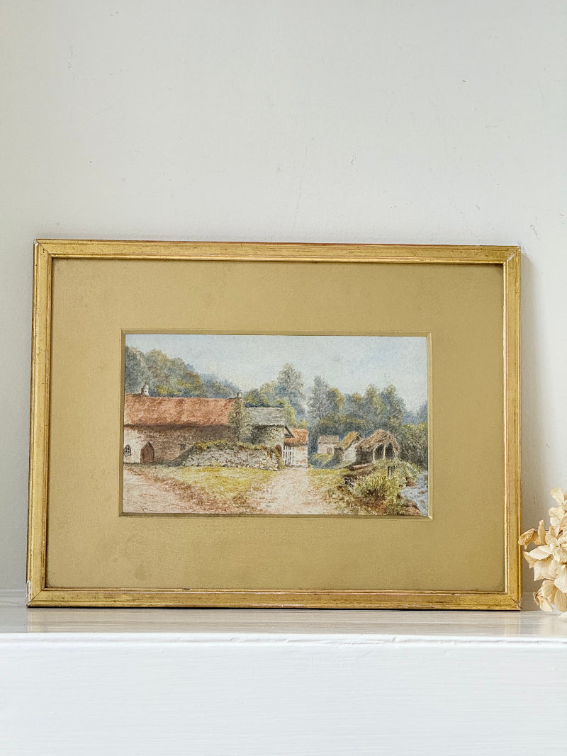 Framed vintage watercolour of countryside farm buildings with red roofs in gold frame photographed on a white surface