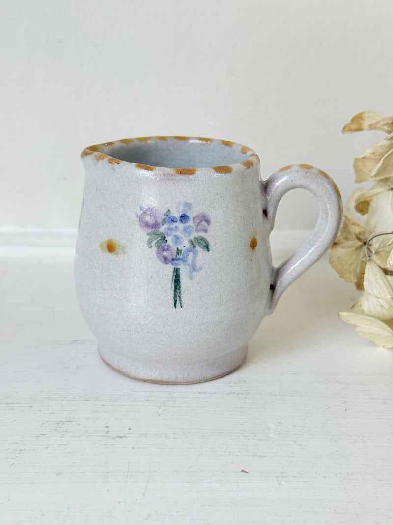 vintage studio pottery milk jug with hand painted lilac flowers and ochre rim photographed on white surface
