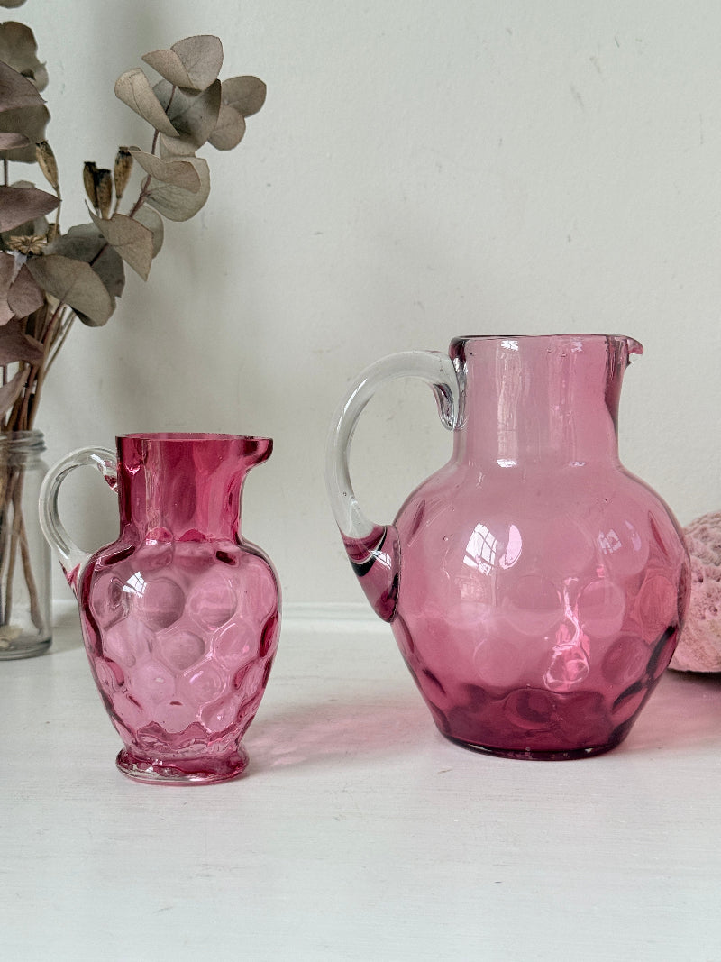 Vintage cranberry glass jugs, a pair with clear handles, photographed on a white surface