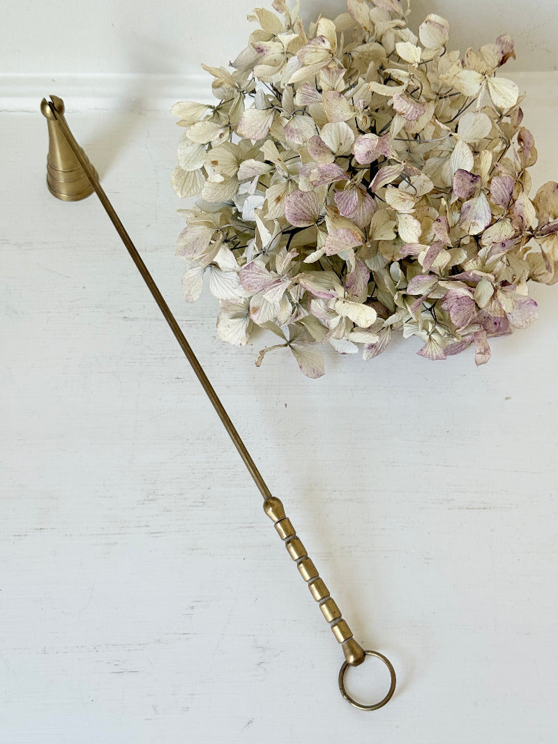 vintage brass candle snuffer with twisted handle and cone-shaped head photographed on white surface