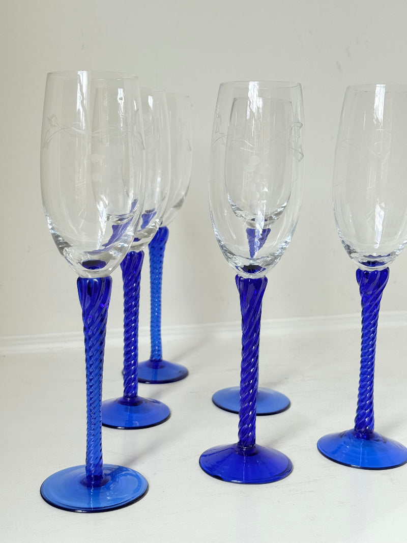 Set of six vintage French champagne flutes with tall clear bowls and cobalt blue twisted stems, photographed on white surface.