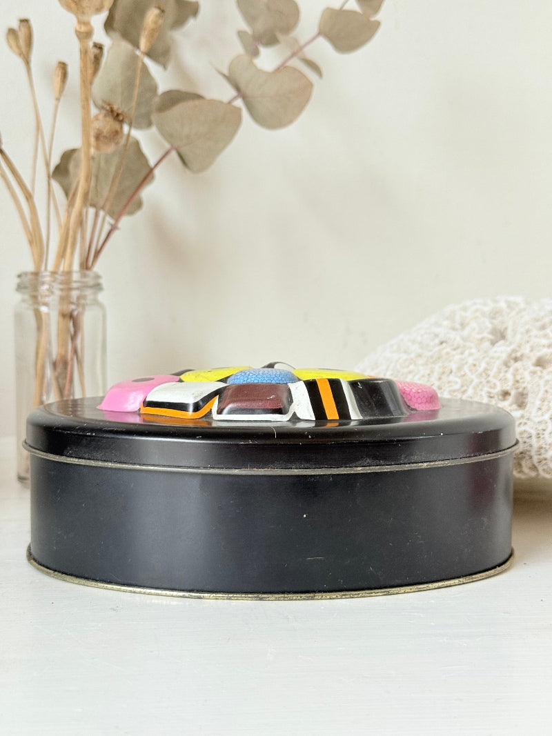 Vintage Liquorice Allsorts decorative tin with raised multicolour sweet design on black base, photographed on white surface.