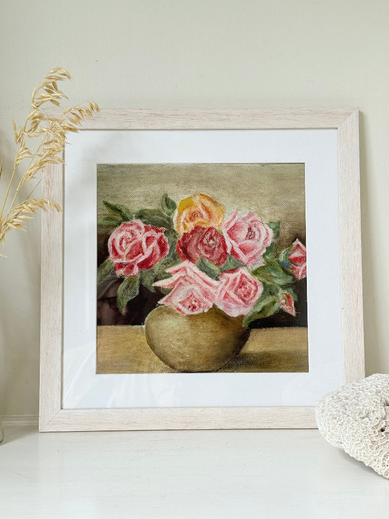 Framed original rose still life painting in pink and yellow, photographed on a white surface.