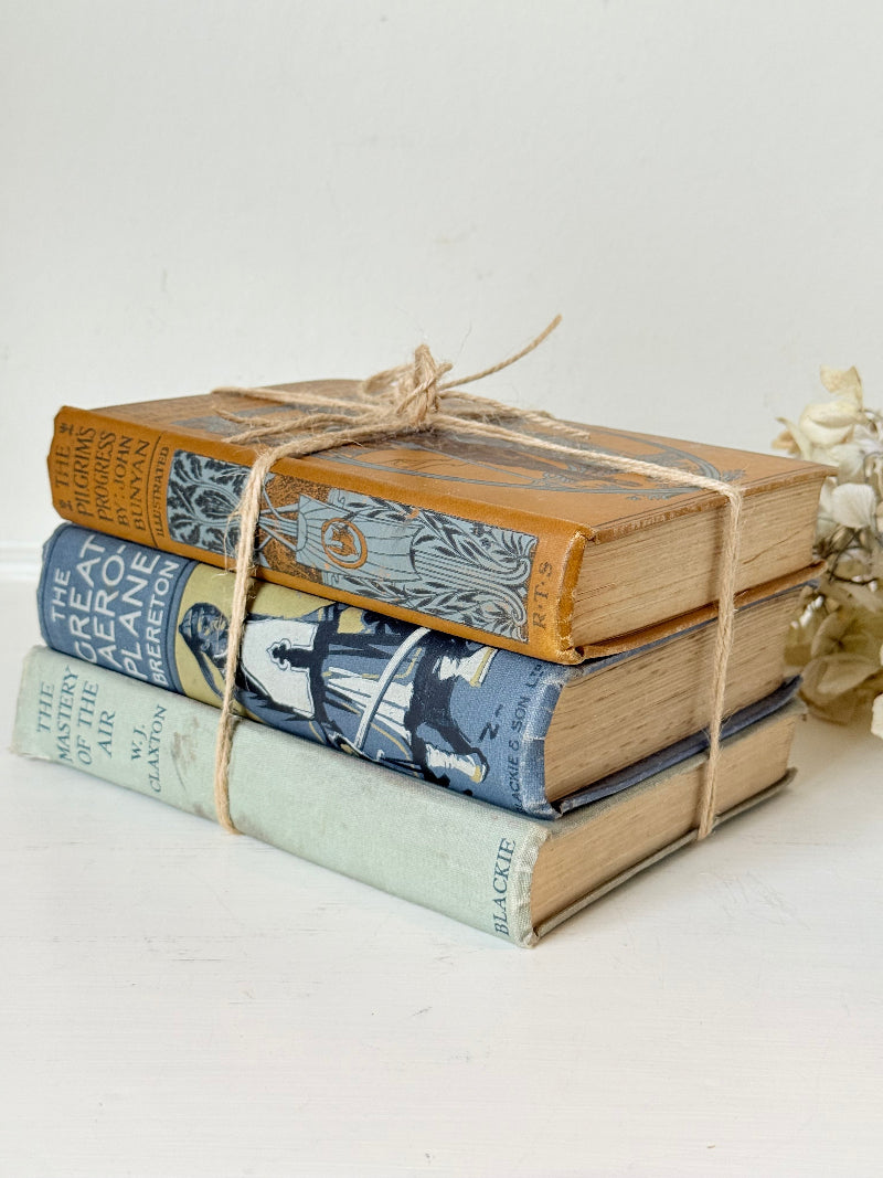 Vintage decorative book bundle in blue, grey, and ochre tied with twine, photographed on a white surface