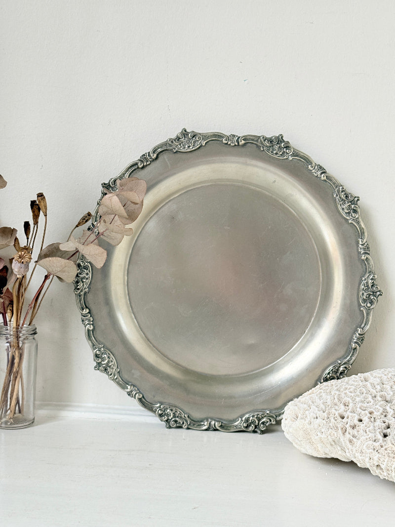 Vintage silvertone metal tray with ornate border, photographed on a white surface