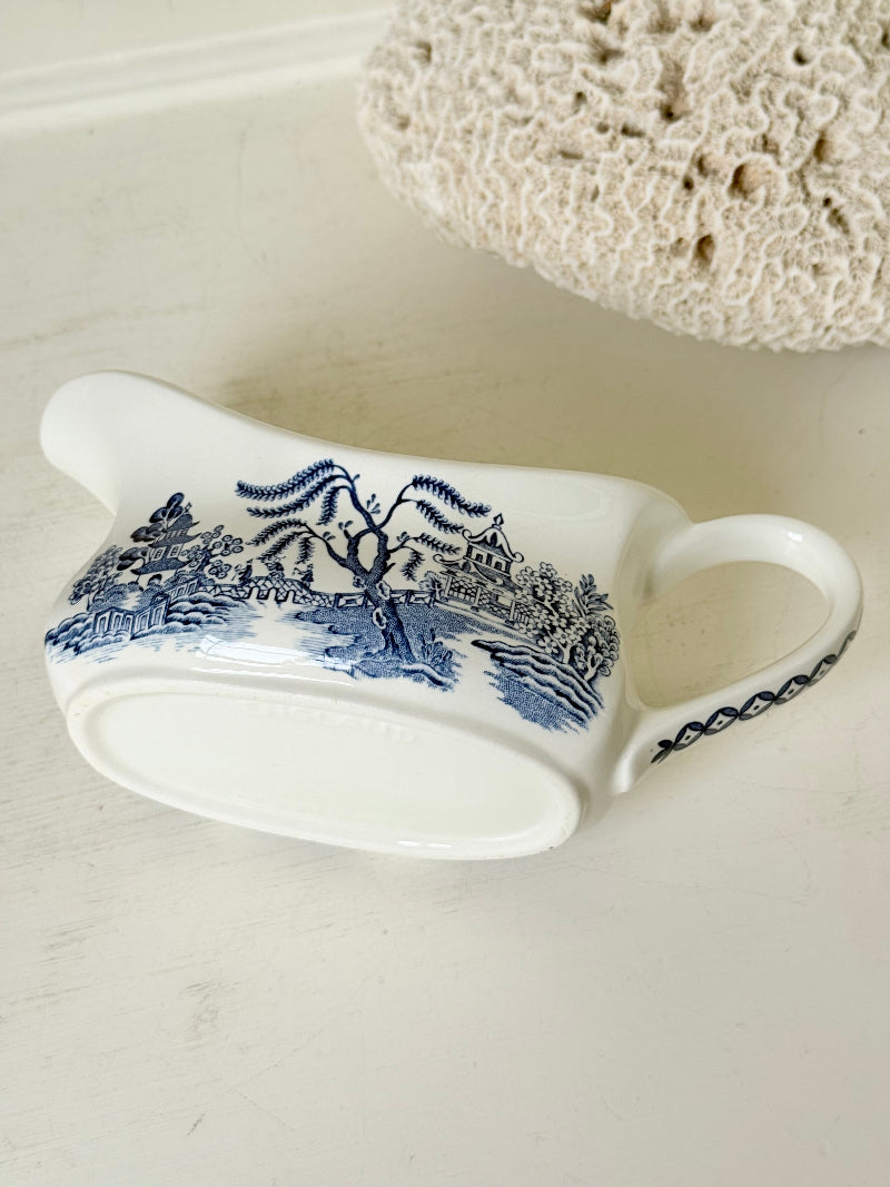 Vintage blue and white ceramic sauce boat with willow pattern photographed on a white surface