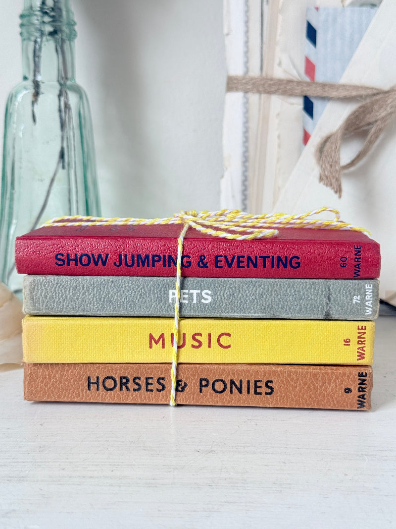 A stack of four small hardcover books tied with a yellow-and-white string, placed on a light surface. The visible titles are &