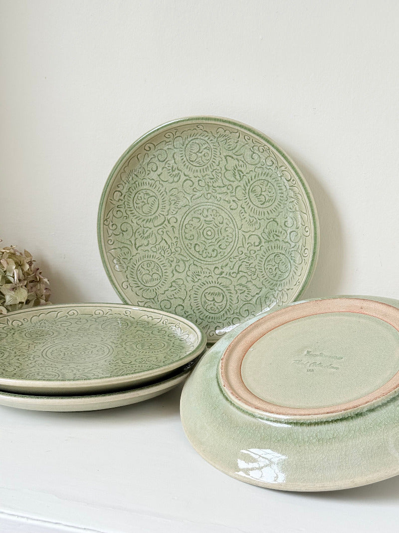 Set of four large Thai celadon stoneware plates in soft green glaze with raised pattern, photographed on a white surface