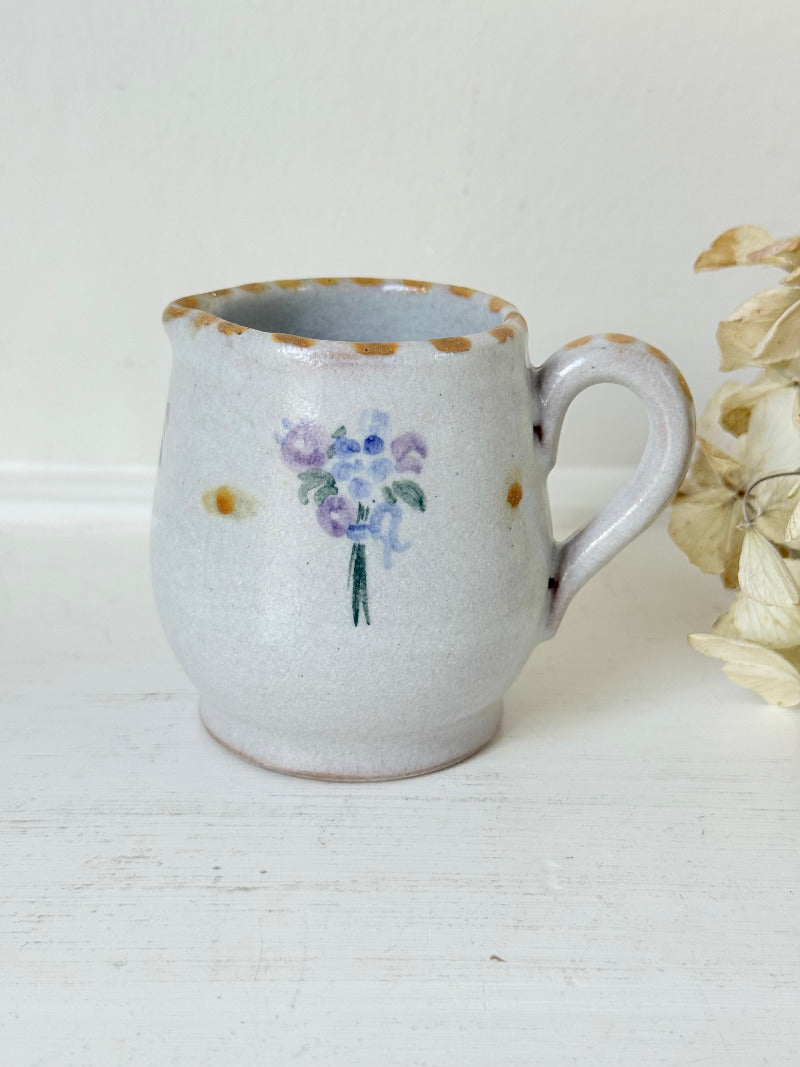 vintage studio pottery milk jug with hand painted lilac flowers and ochre rim photographed on white surface