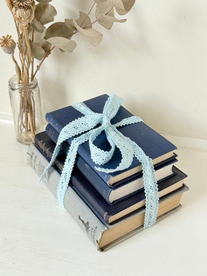 Vintage navy decorative book bundle tied with pale blue lace ribbon, photographed on a white surface