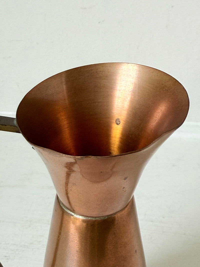 Vintage copper and brass jug with slender handle, photographed on a white surface