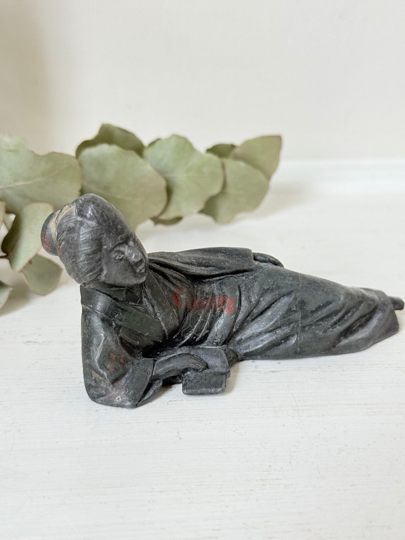 antique japanese bronze reclining lady with impressed marks to base photographed on white surface with foliage background