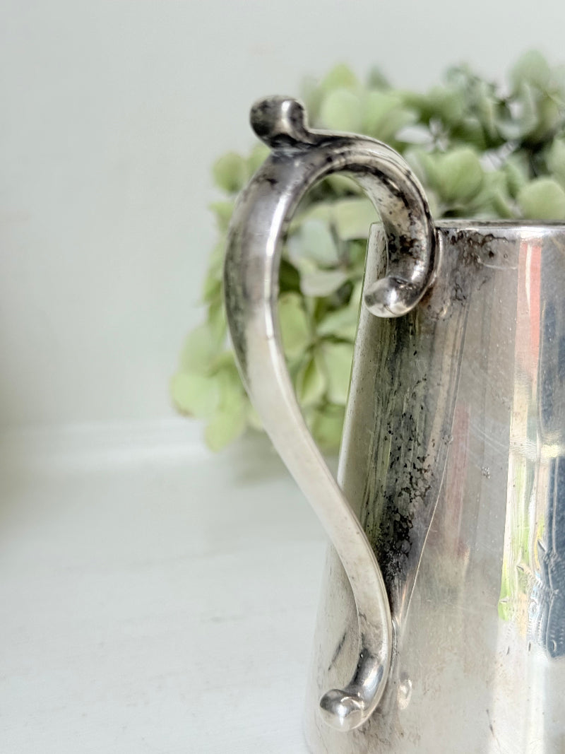 vintage silver plate jug with curved handle photographed on white surface with green hydrangeas