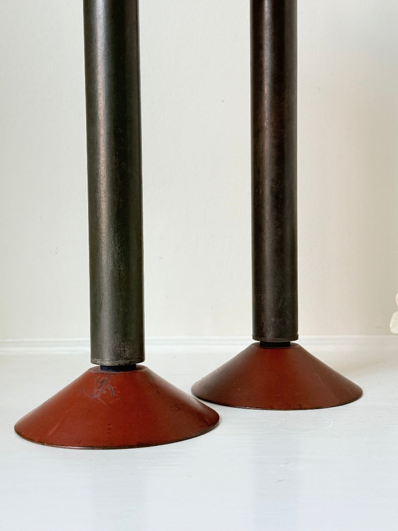 Pair of tall vintage metal candlesticks in black and burgundy, styled with white taper candles on a white surface.