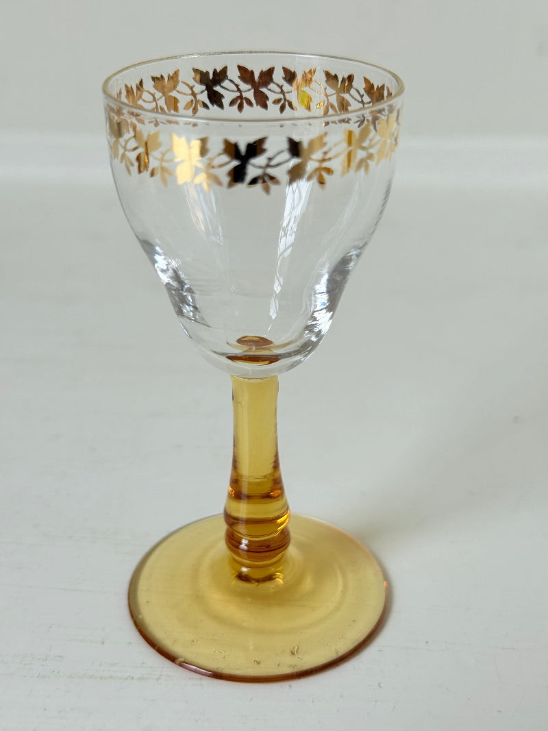 Vintage set of four shot glasses with amber stems and gilt rims, photographed on a white surface